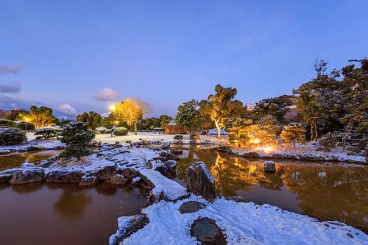 Snow covered stone bridge over pond in Japanese garden at dawn. High quality photo