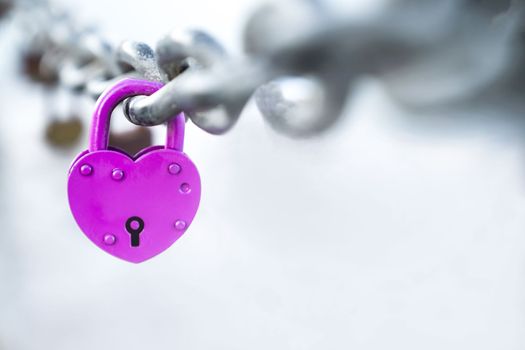 Pink heart shaped lock hangs from bridge chain, wedding custom is symbol of eternal love, copy space
