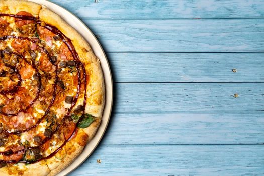 Delicious large pizza with bacon and spinach on a blue wooden background.