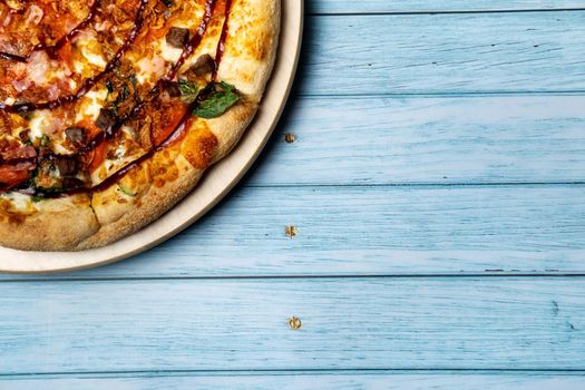 Delicious large pizza with bacon and spinach on a blue wooden background.