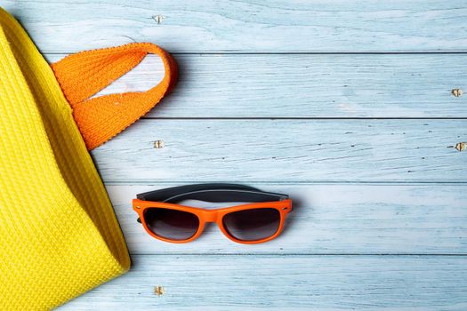 An empty bag with a handle and sunglasses lying on a blue wooden background.