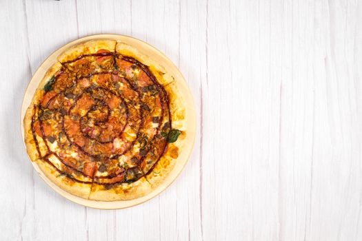 Delicious large pizza with bacon and spinach on a light wooden background.