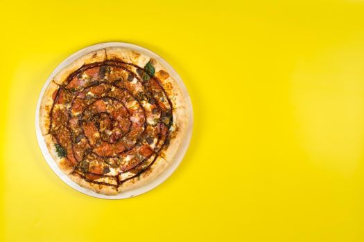 Delicious large pizza with bacon and spinach on a yellow background.