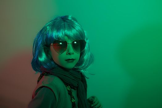 A glamour little girl posing for a photo portrait while wearing a colorful wig on green background