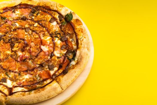 Delicious large pizza with bacon and spinach on a yellow background.