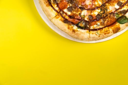Delicious large pizza with bacon and spinach on a yellow background.