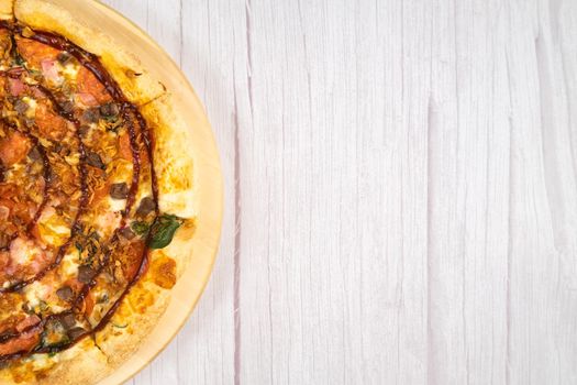 Delicious large pizza with bacon and spinach on a light wooden background.