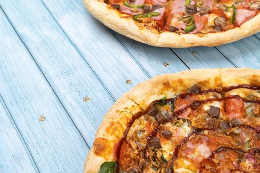 Two different delicious big pizzas on a blue wooden background.