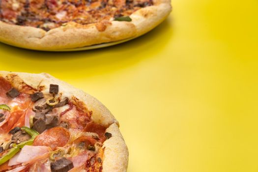 Two different Delicious big pizzas on a yellow background.