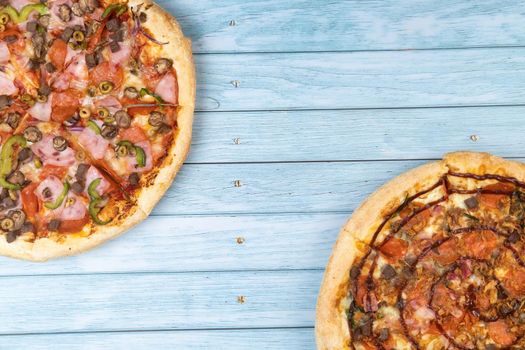 Two different delicious big pizzas on a blue wooden background.