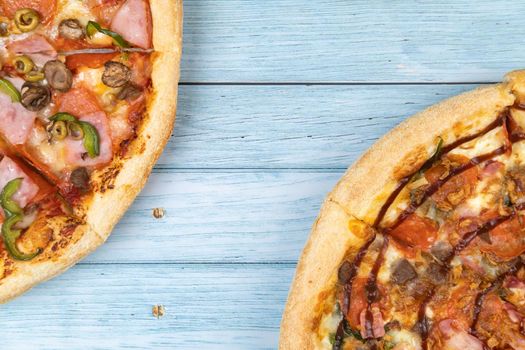 Two different delicious big pizzas on a blue wooden background.