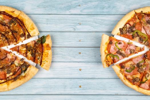 Two different delicious big pizzas on a blue wooden background.