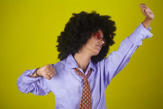 A beautiful young woman with afro curly hairstyle wearing male clothes and stretching on yellow background