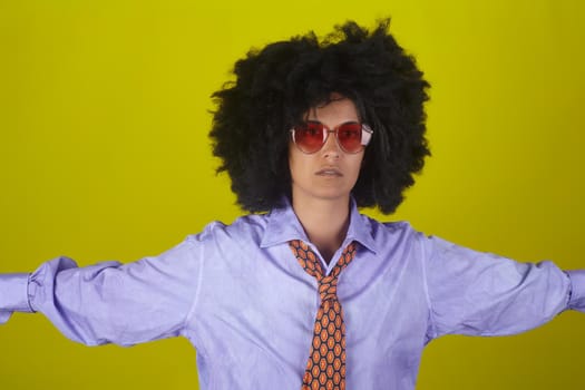 A beautiful woman with afro curly hairstyle wearing sunglasses, male shirt and necktie on yellow background