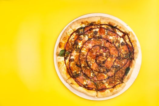 Delicious large pizza with bacon and spinach on a yellow background.