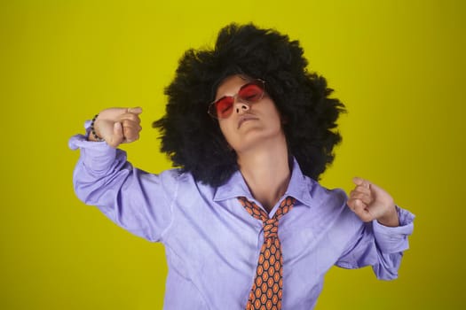 A beautiful young woman with afro curly hairstyle wearing male clothes and stretching on yellow background