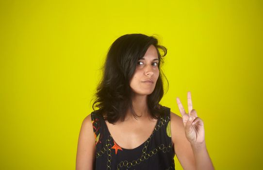 Portrait of an Indian woman showing fingers doing victory sign or number two on yellow background