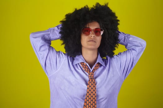 A beautiful woman with afro curly hairstyle wearing sunglasses, male shirt and necktie on yellow background