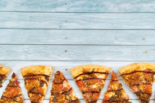 Lots of delicious triangular pizza slices on a blue wooden background.