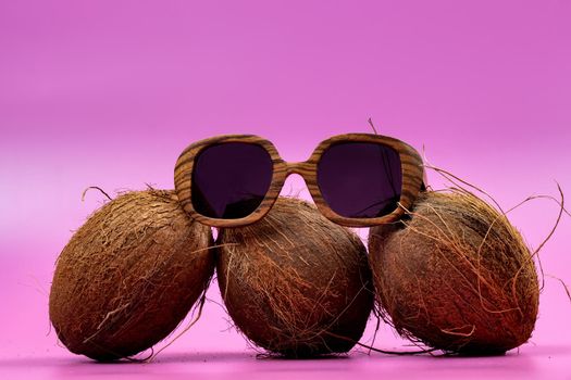 three whole coconuts and wooden glasses on a pink background.