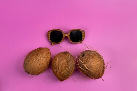 three whole coconuts and wooden glasses on a pink background.
