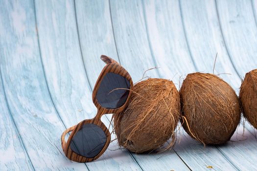 three whole coconuts and wooden glasses on a blue wooden background.