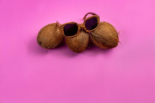 three whole coconuts and wooden glasses on a pink background.