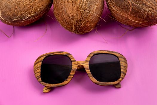three whole coconuts and wooden glasses on a pink background.