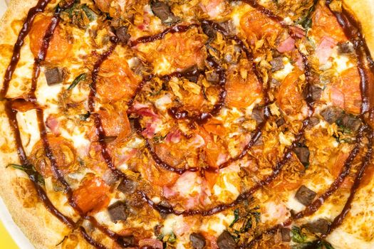 Delicious large pizza with bacon and spinach on a yellow background.