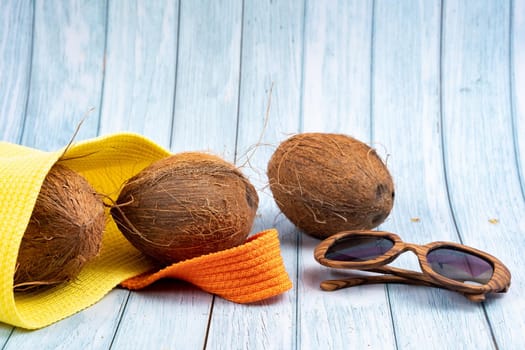 Whole coconuts lying in a yellow bag and glasses on a blue wooden background.