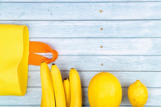 Yellow bag and bananas, melon and lemon on blue wooden background.