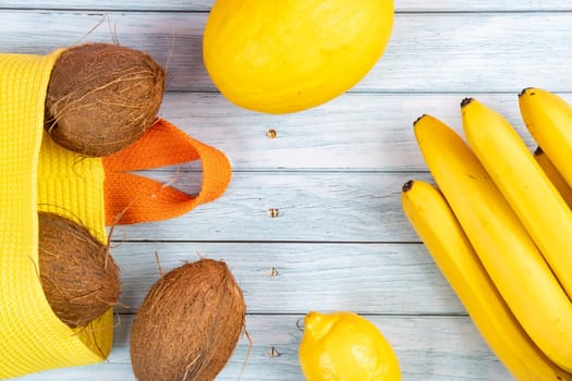 Whole coconuts in a yellow bag, bananas and melon on a blue wooden background.