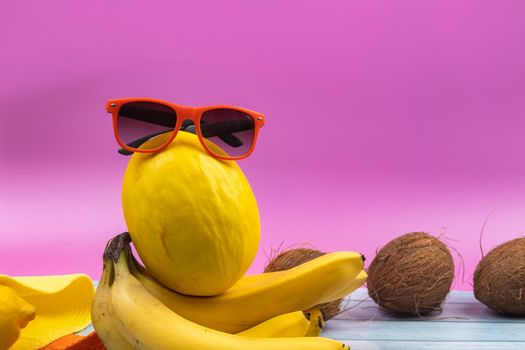 An assortment of yellow fruits and glasses lies on a pink background.