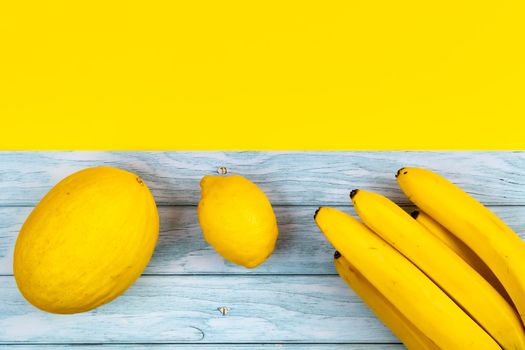 An assortment of yellow fruits lies on a blue wooden background and a yellow background.