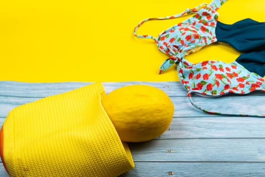 Top view of a swimsuit and a melon in a bag, lying on a blue wooden and yellow background.Summer vacation concept.