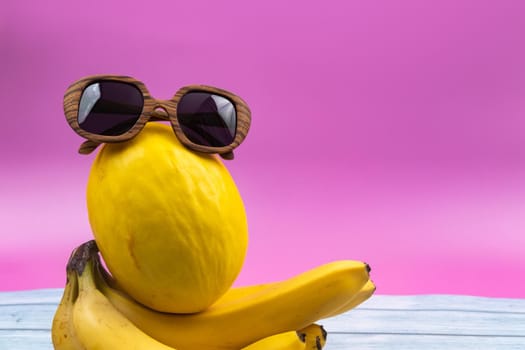 An assortment of yellow fruits and glasses lies on a pink background.