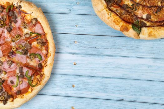 Two different delicious big pizzas on a blue wooden background.