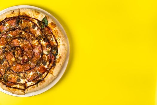 Delicious large pizza with bacon and spinach on a yellow background.