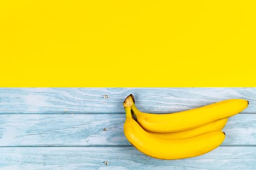 Yellow bananas lie on a blue wooden background and a yellow background.
