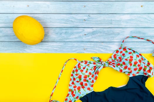 Top view of a swimsuit and a melon lying on a blue wooden and yellow background.Summer vacation concept.