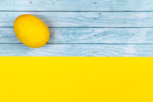 A whole yellow melon lies on a blue wooden background and a yellow background.