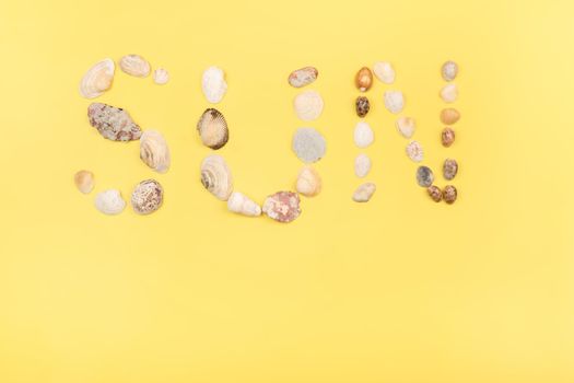 The inscription of the word sun is made of shells on a yellow background.Travel concept.