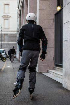 Rear view of a man wearing helmet and knee pads on rollerblade skates riding outdoors on urban street