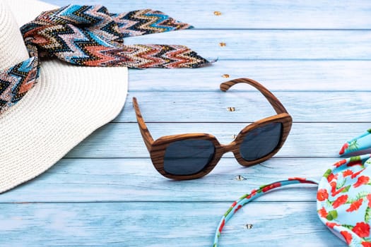 Top view of a straw white hat with glasses and a swimsuit, lying on a blue wooden background.Summer vacation concept.