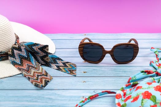 Top view of a straw white hat with glasses and a swimsuit, lying on a blue wooden background.Summer vacation concept.
