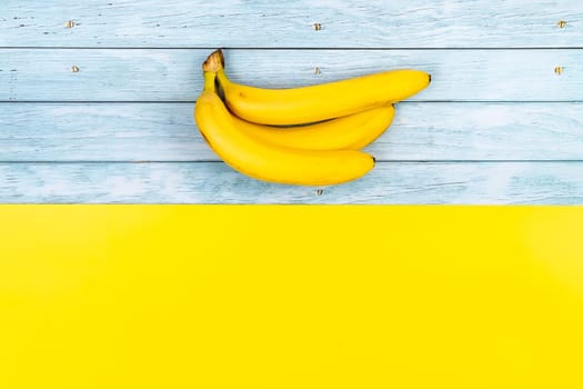 Yellow bananas lie on a blue wooden background and a yellow background.