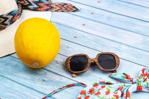 Top view of a straw white hat with glasses and a swimsuit, lying on a blue wooden background.Summer vacation concept.