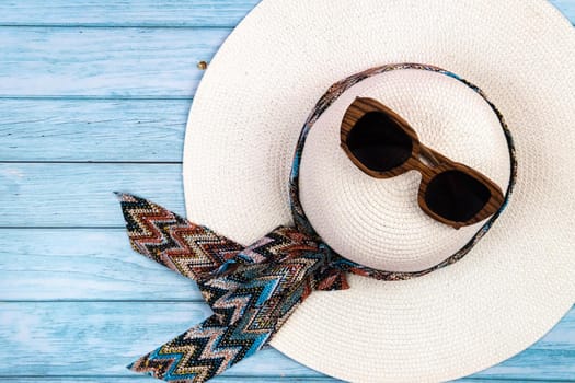 Top view of a straw white hat with glasses lying on a blue wooden background.Summer vacation concept.