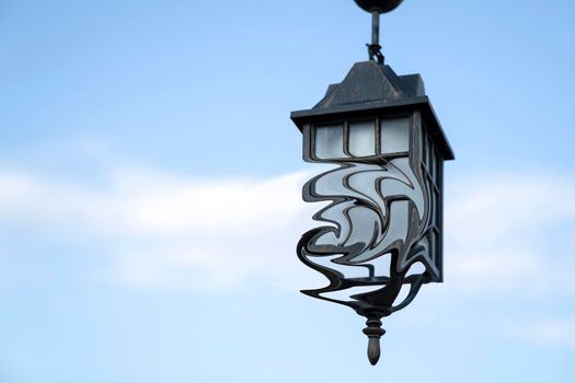 Ancient street lamp with distorted form on background blue sky, close up. Copy space.