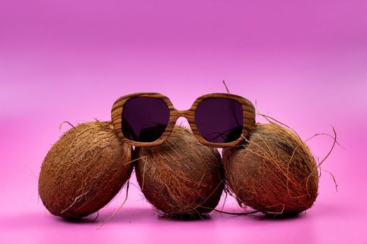 three whole coconuts and wooden glasses on a pink background.
